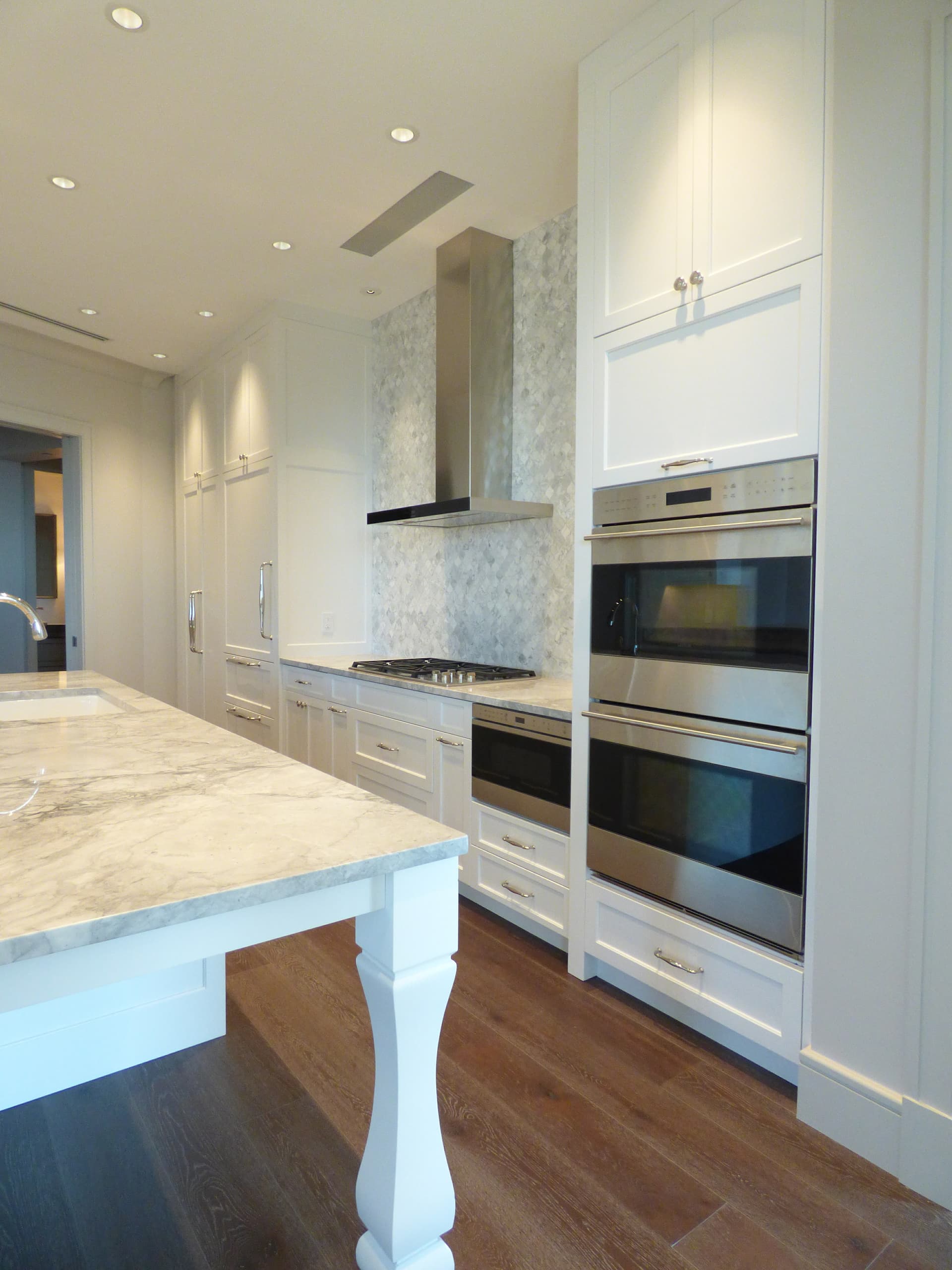 White custom kitchen cabinets with double wall ovens and a marble island built by Hdez Gabinets