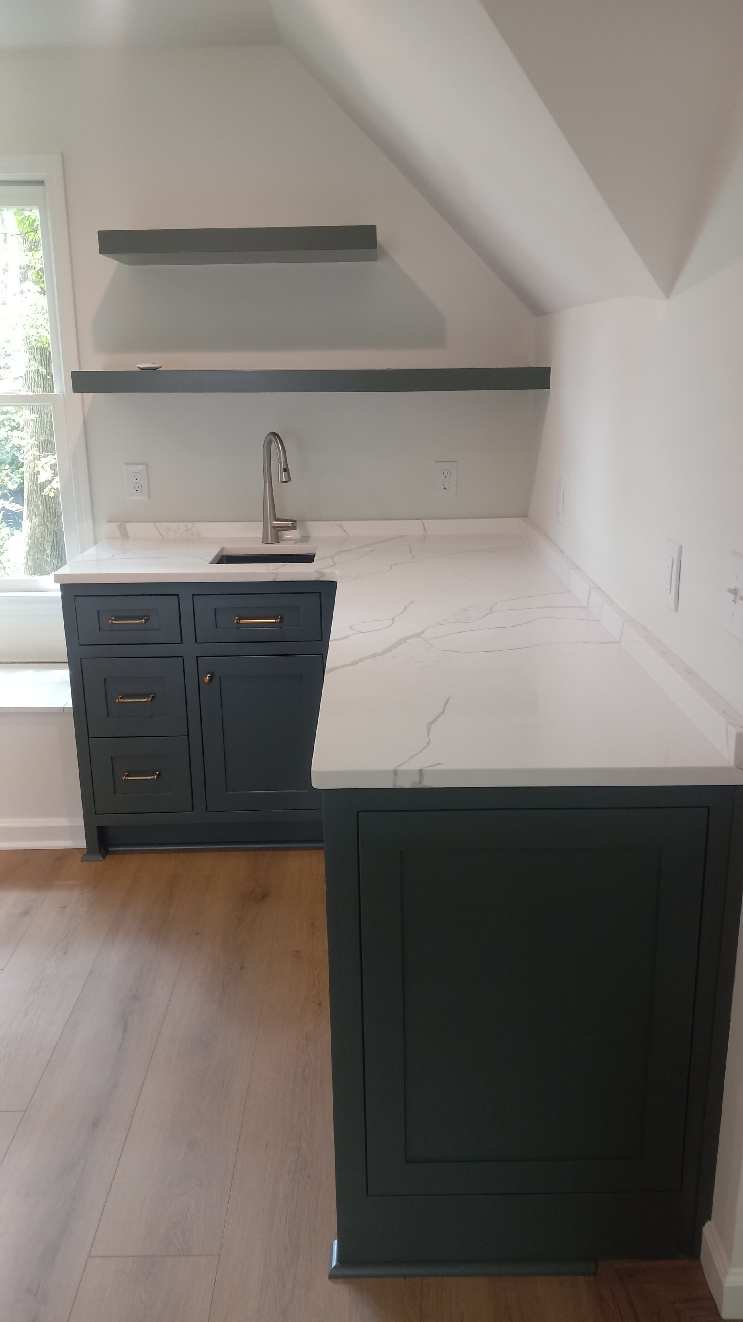 Navy inset cabinets with brass pulls and floating shelves under a sloped ceiling, built by Hdez Gabinets