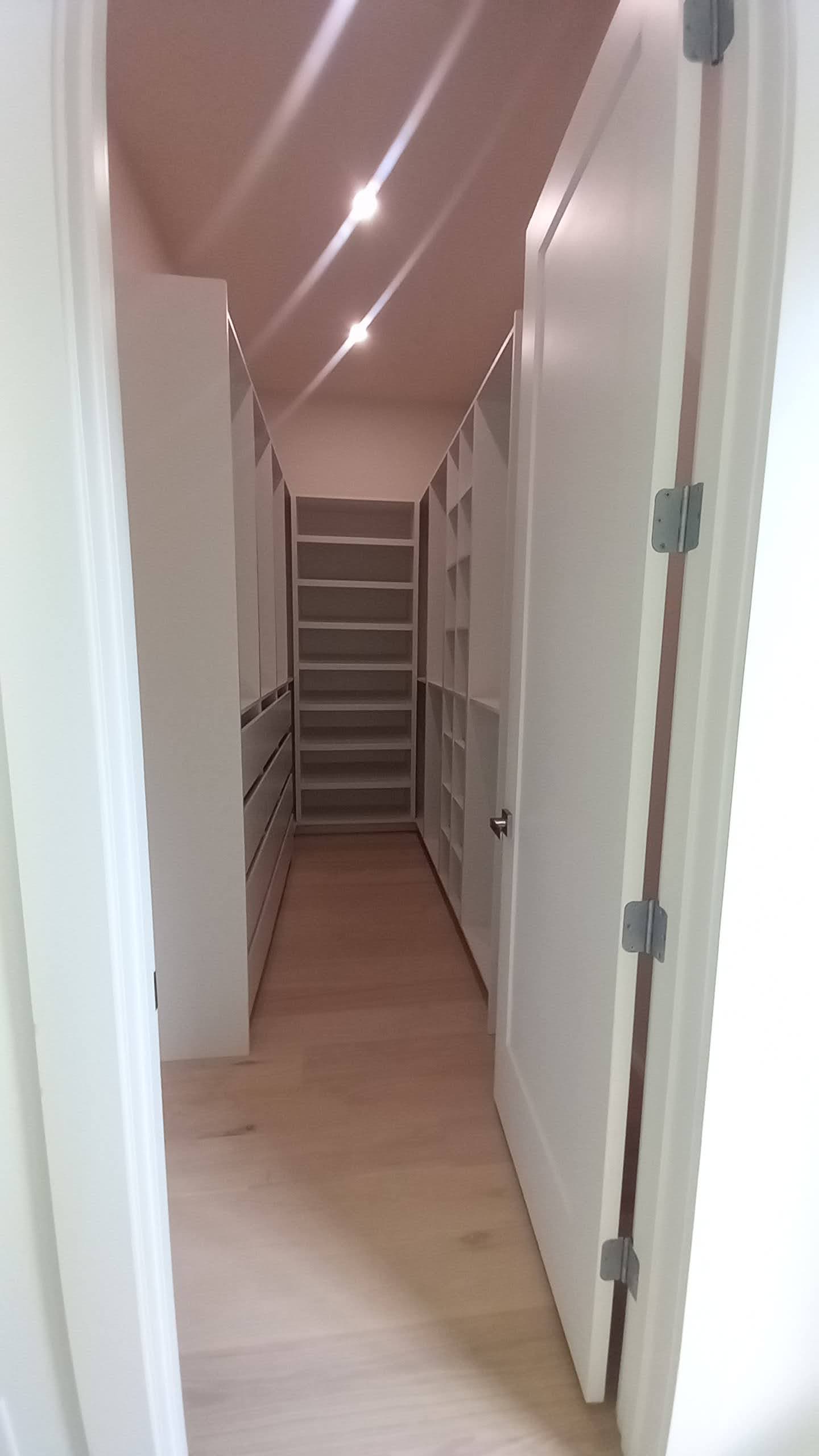 Narrow walk-in closet with white shelving and drawers that follows a sloped ceiling, built by Hdez Gabinets